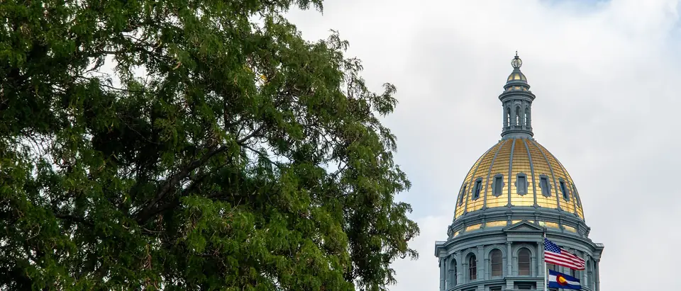 The gold dome of the Colorado State Capitol behind green trees