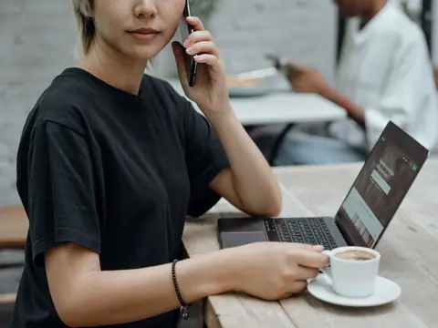 A woman on a call with her laptop open at a cafe table