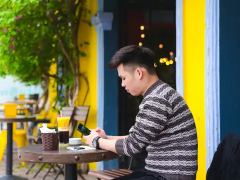 A man checking his phone at a sidewalk cafe table