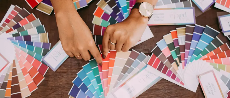 Hands sorting through fans of paint color swatches on a table