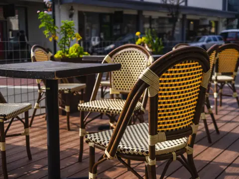Wicker cafe chairs on a sidewalk patio on a sunny day