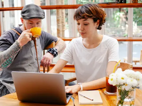 Two business owners planning at a laptop in a sunny cafe