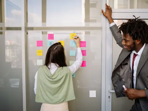 Two people planning with sticky notes on a glass wall in a bright office