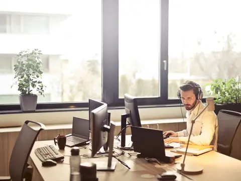 A man working at a computer in a bright office with tall windows