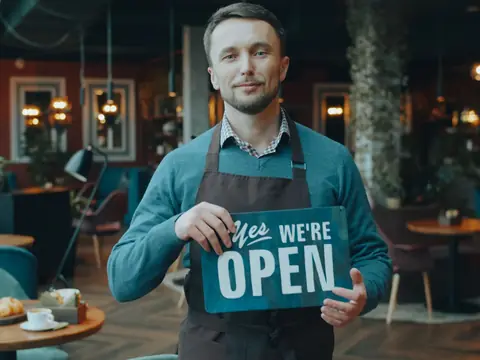 A cafe owner holding an open sign in his shop