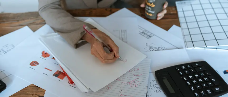 Writing notes at a desk beside a calculator and printed pages