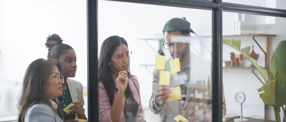 A small team planning with sticky notes behind an office glass wall