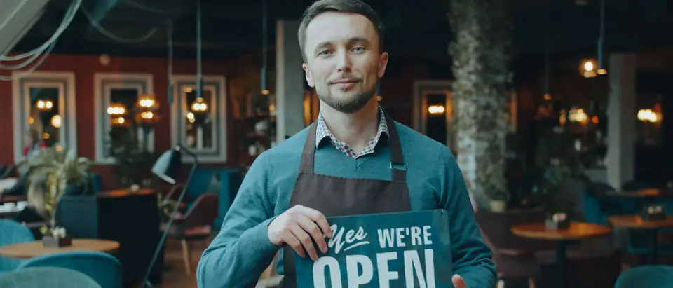 A cafe owner holding an open sign in his shop