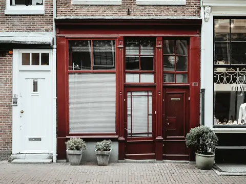 A red shop front on a brick building with potted plants by the door