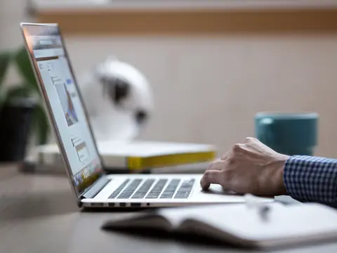 A laptop open on a desk beside a notebook and a coffee mug