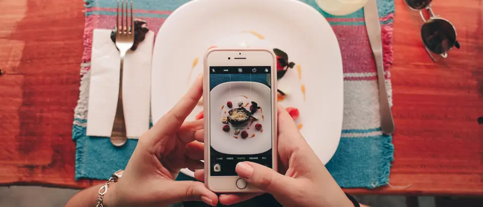 Taking a phone photo of a plated dessert on a colorful restaurant table