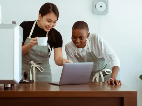 Two cafe owners looking at their website on a laptop behind the counter
