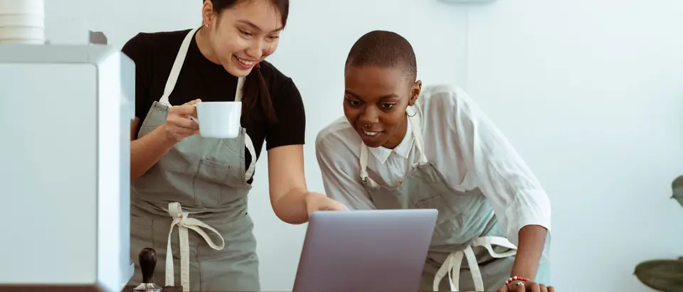 Two cafe owners looking at their website on a laptop behind the counter