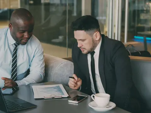 Two men going over a printed report beside a laptop and coffee
