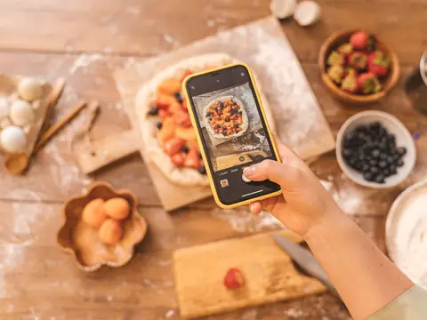 Photographing a fruit pastry on a phone at a sunny table