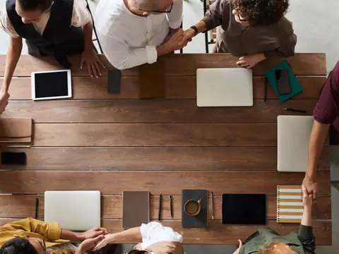 A small team planning around a wooden table with laptops, seen from above