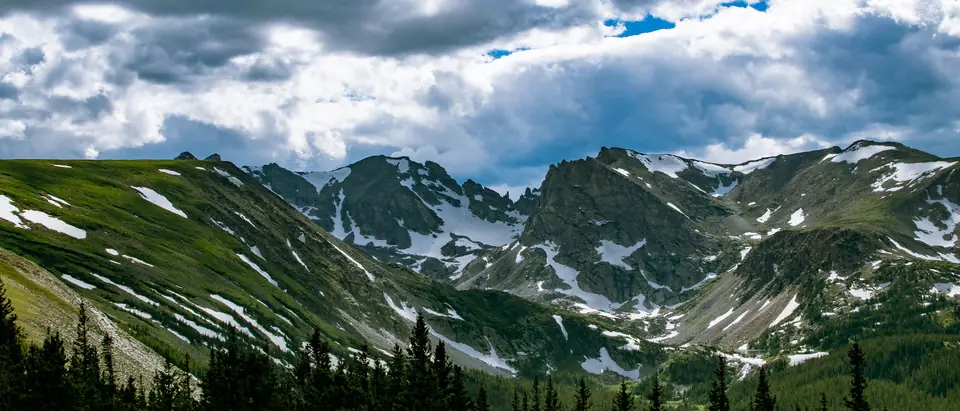 Snow-streaked green mountains under a bright blue sky with clouds
