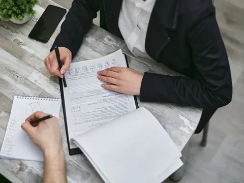 Taking notes beside a clipboard of papers at a table, seen from above